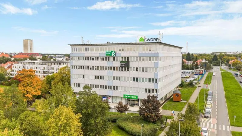 Bílá kancelářská budova SWORP obklopená zelení a parkovištěm na slunečný den.